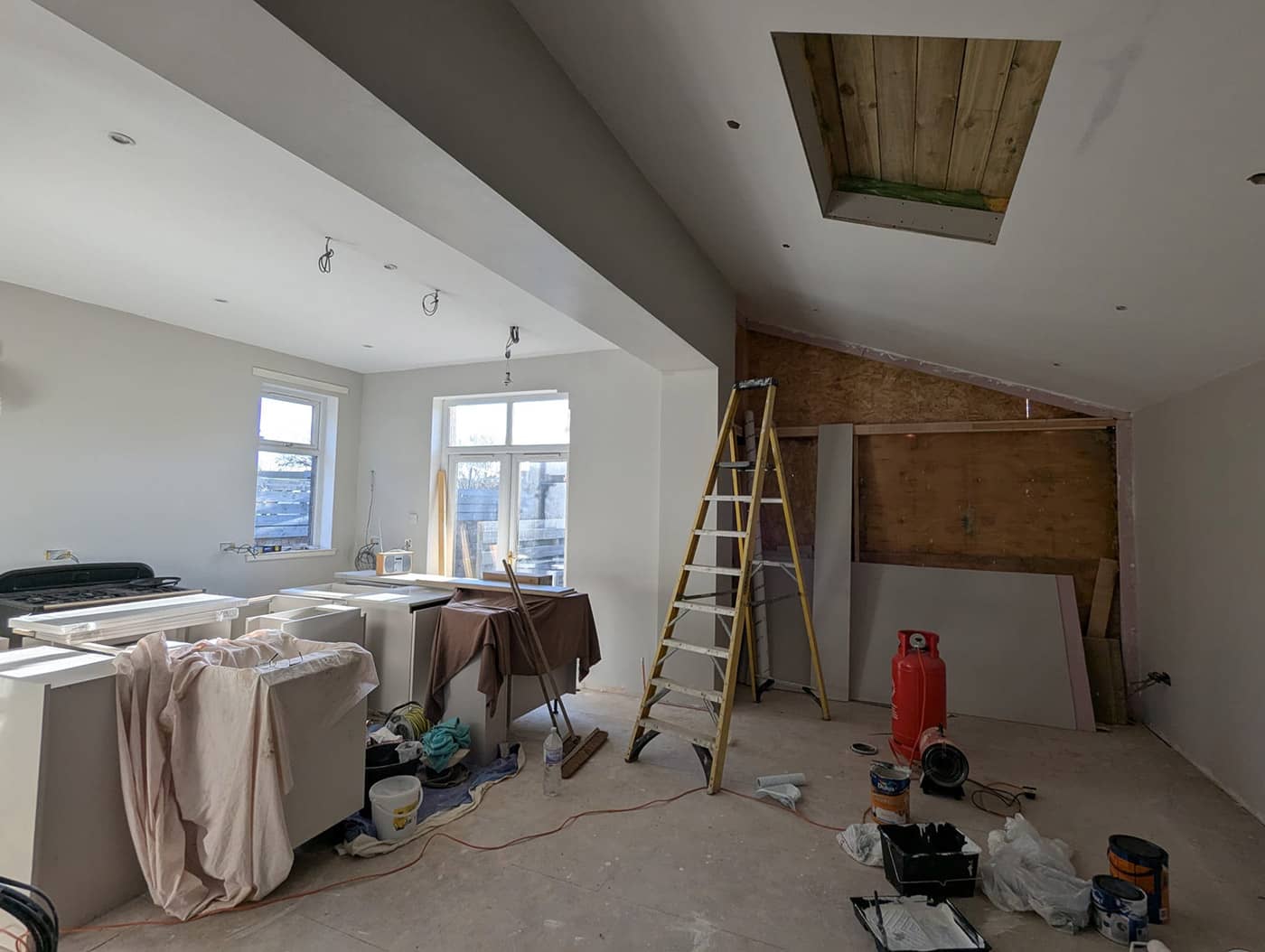Extension interior during plastering, with the opening into the existing kitchen, a roof light opening and timber sheathing still visible on one wall